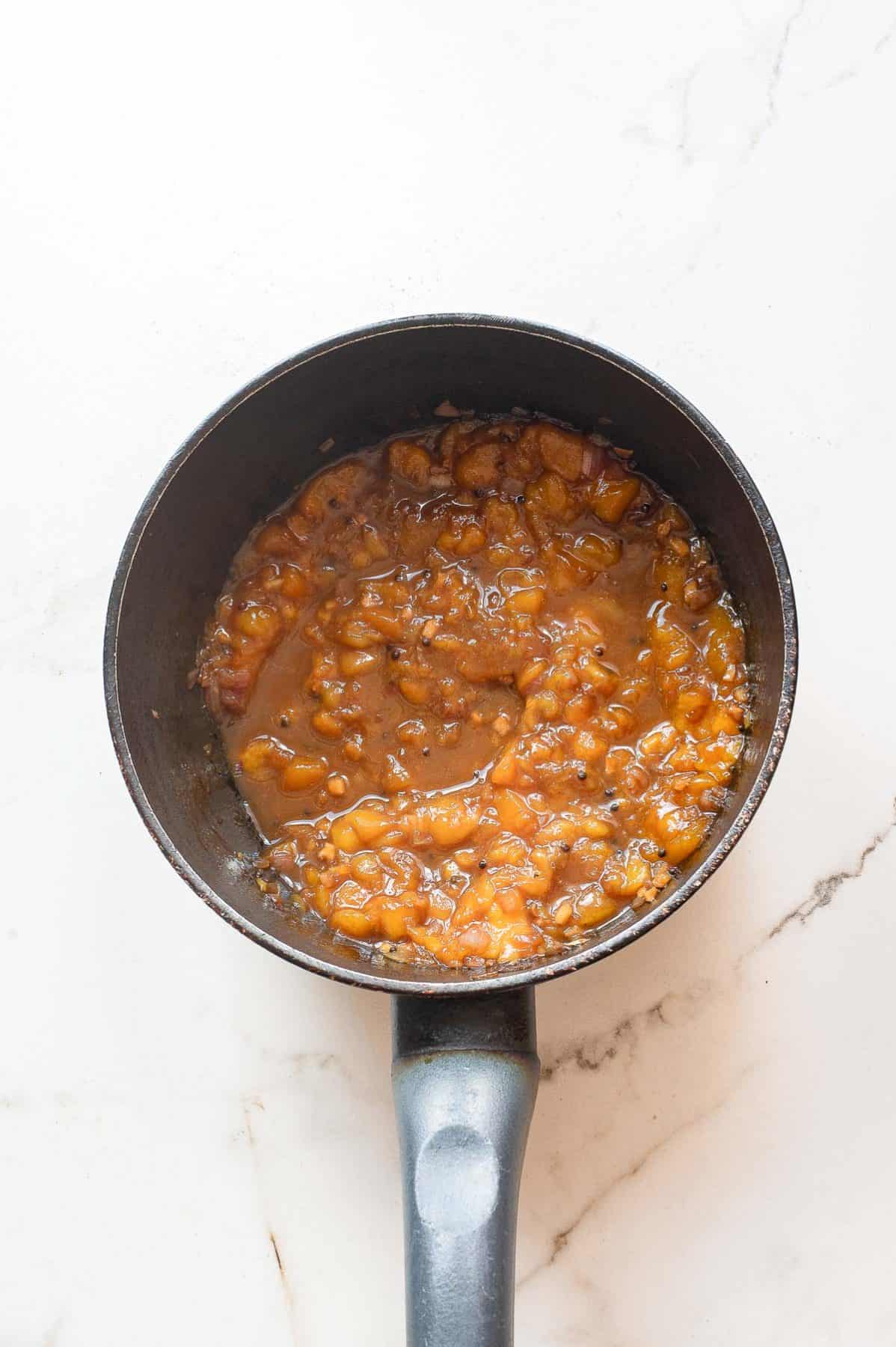 A small saucepan containing a thick, chunky orange-brown sauce or mixture sits on a white marble surface.