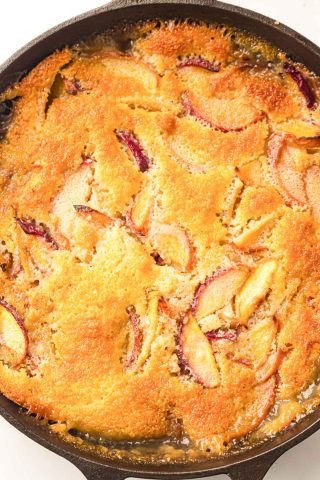 A close-up of a baked peach cobbler in a cast iron skillet, showing a golden-brown crust with visible peach slices.