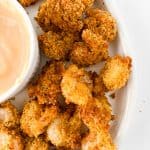 A plate of breaded popcorn shrimp served with a side of dipping sauce.